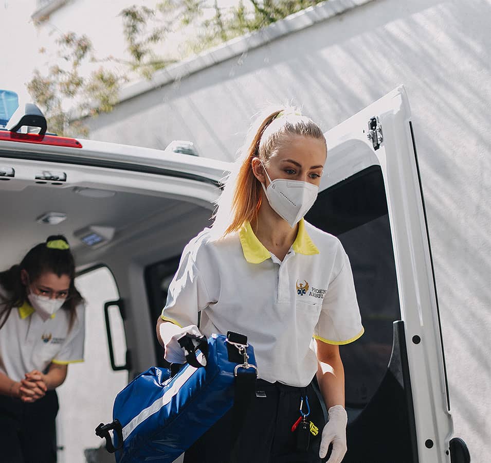 Zwei junge Rettungssanitäter steigen mit Ausrüstung aus der Rückseite eines Krankenwagens